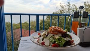 a plate of salad with shrimp and tomatoes on a table with a blue railing